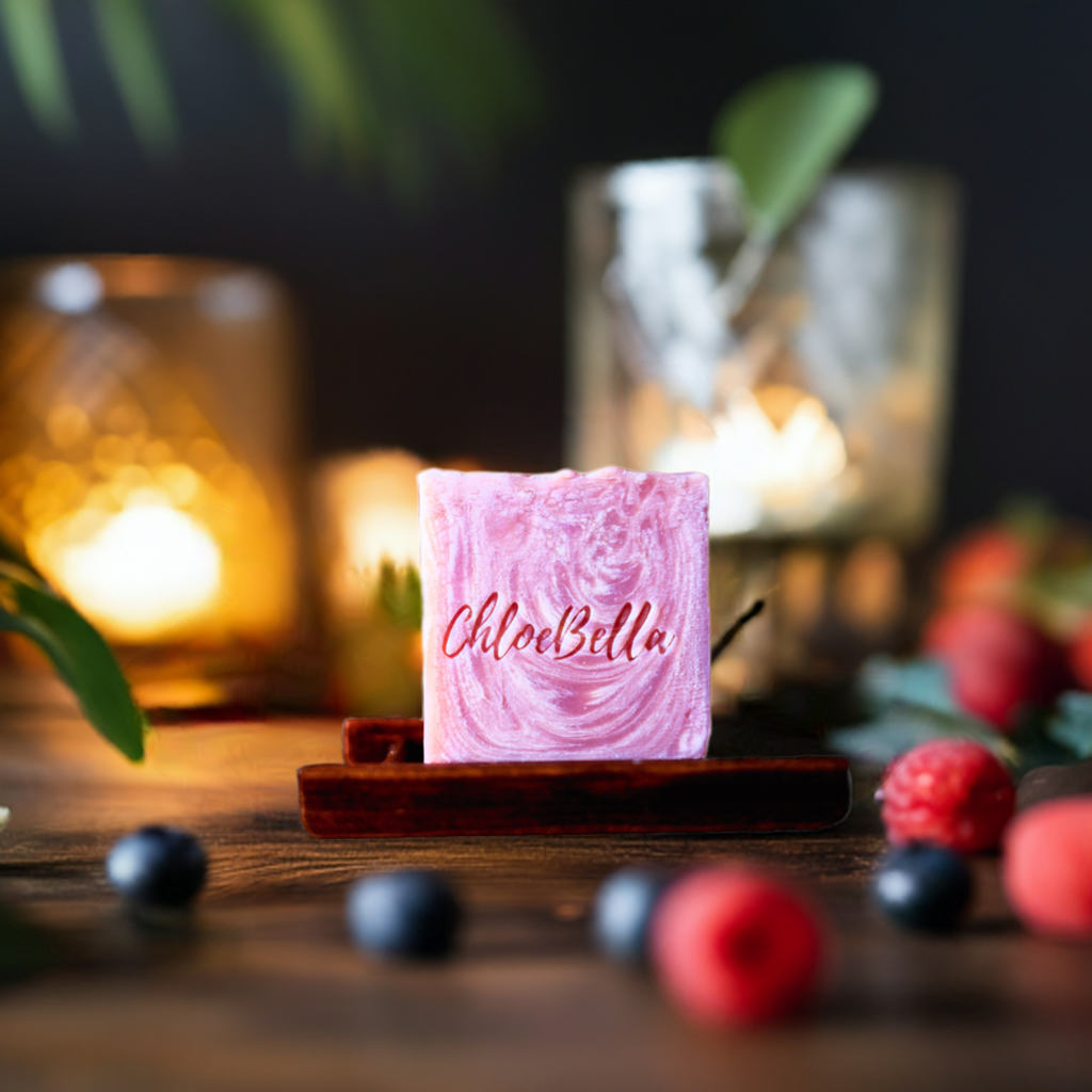 Handcrafted luxury berry scented soap sitting on a wooden stand surrounded by strawberries, raspberries, and blue berries.
