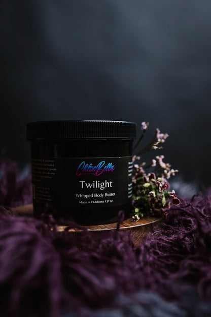 Black container of 'Twilight Whipped Body Butter' on a dark background with purple flowers.